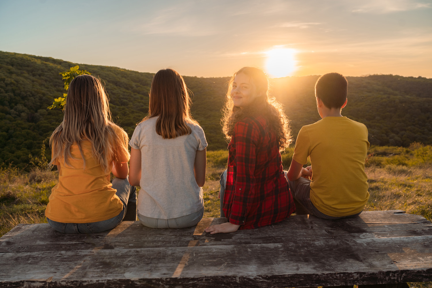 Vier Jugendliche auf einem Holzpodest im Sonnenuntergang – ein Mädchen dreht sich dabei um zur Kamera
